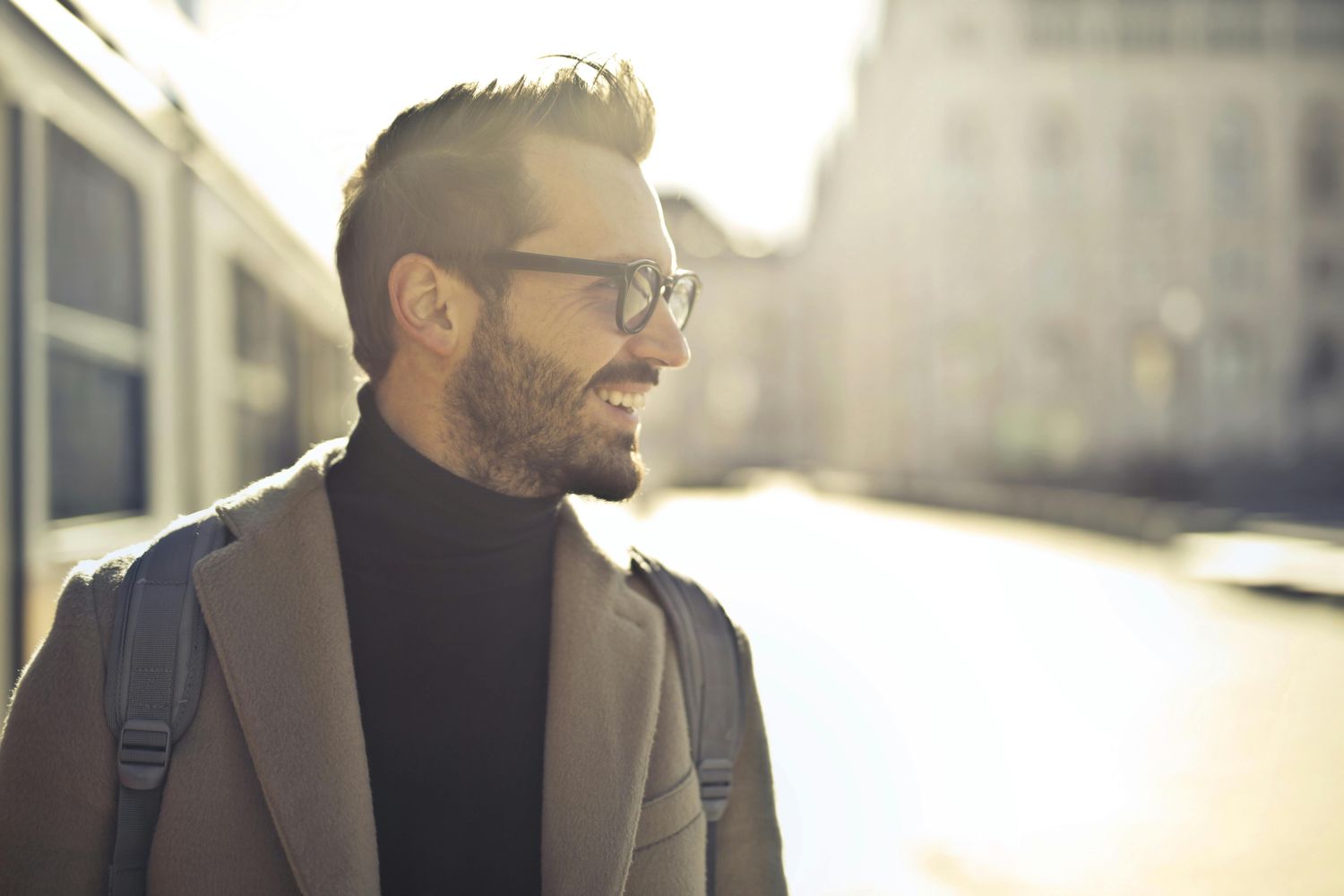 Smiling man in glasses outdoors with sunlight.